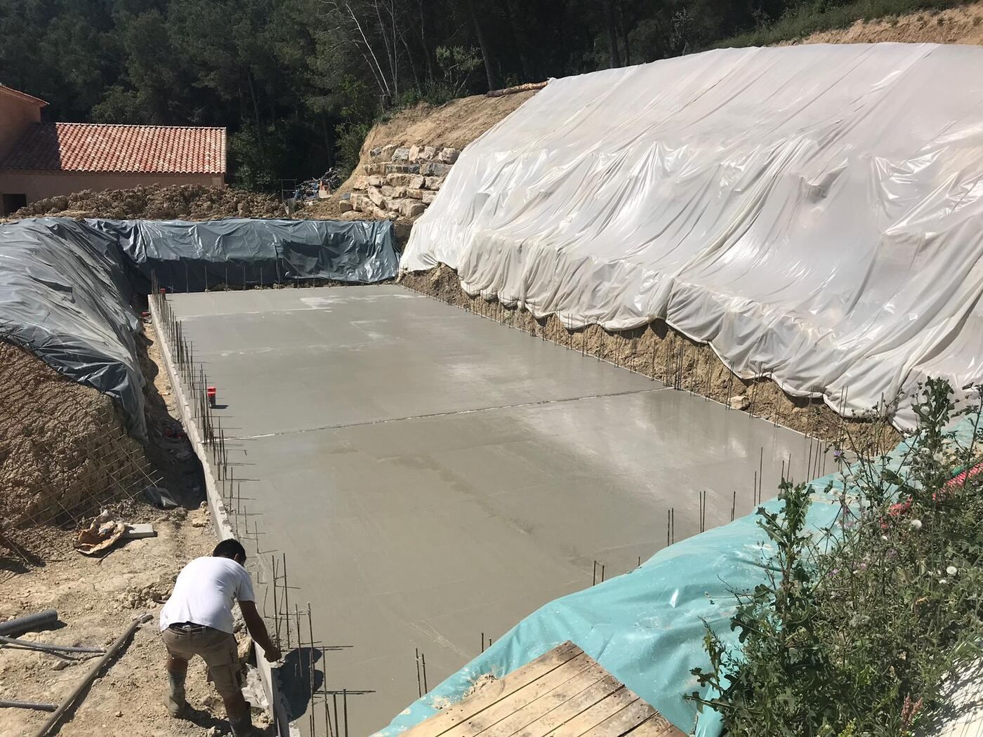 Radier d'une piscine en béton armé fraîchement coulé, attentes des voiles en place